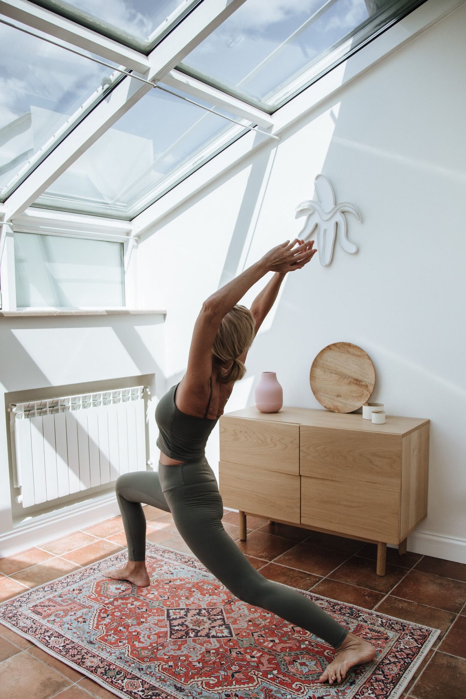 Mulher praticando postura de lunge com abertura de braços em ambiente doméstico iluminado ilustrando a diferença entre Hatha e Vinyasa yoga na prática