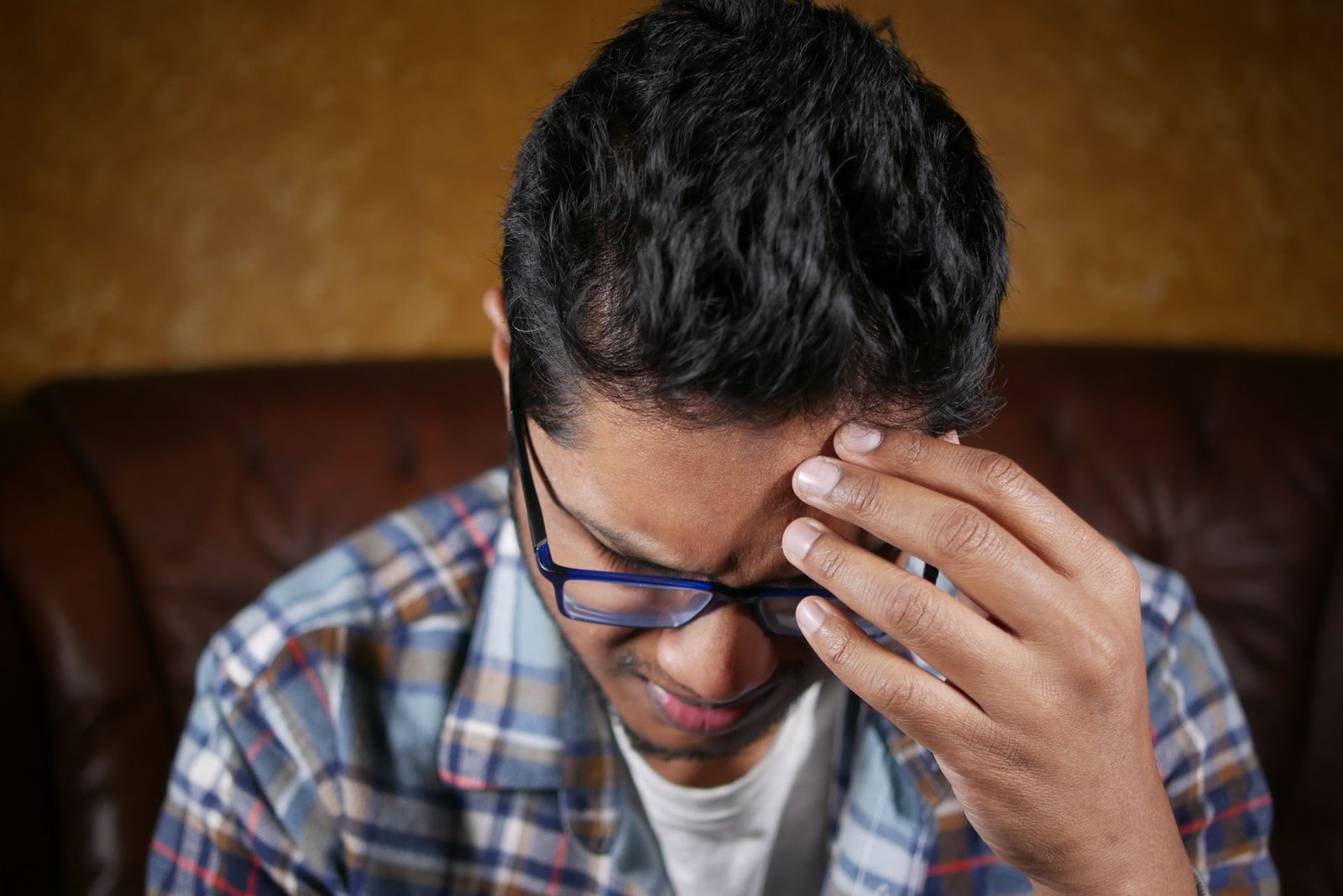 Homem jovem com óculos com a mão na cabeça em expressão de esgotamento e estresse ilustrando cortisol cronicamente elevado e sobrecarga mental no cotidiano