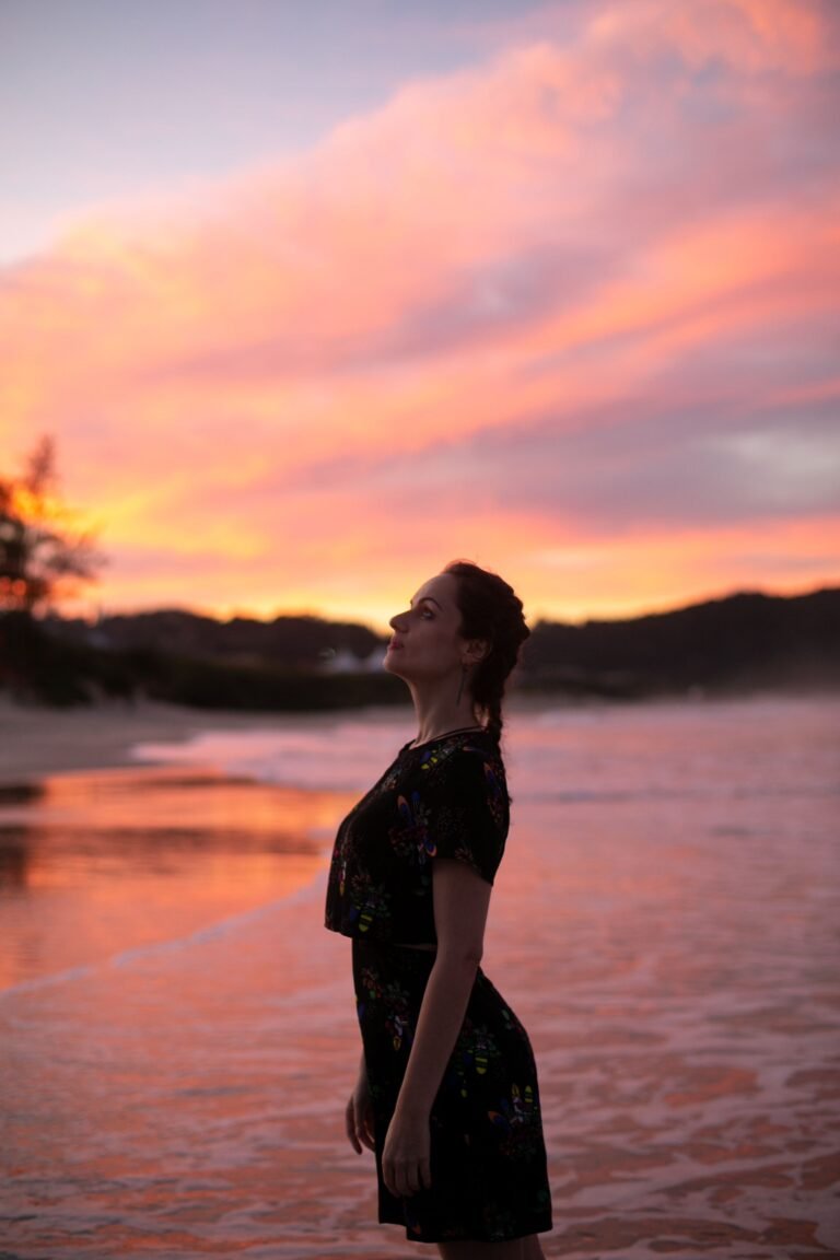 Mulher em contemplação na praia ao pôr do sol com céu laranja, remetendo à prática meditativa no litoral cearense