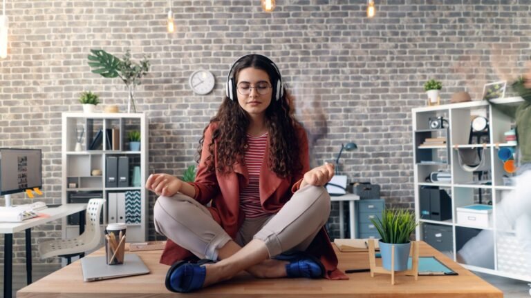 Mulher meditando sentada na mesa do escritório com fones de ouvido praticando yoga no trabalho