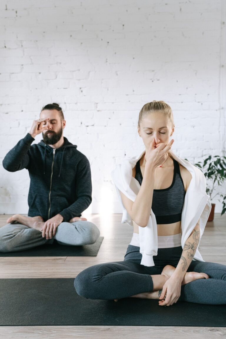 Homem e mulher praticando pranayama com respiração alternada pelas narinas em estúdio de yoga