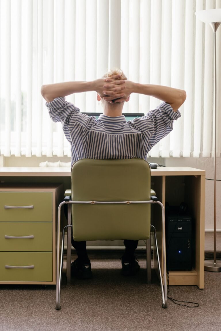 Pessoa sentada na cadeira do escritório com as mãos atrás da cabeça fazendo pausa de alongamento durante home office ilustrando yoga na mesa para aliviar tensão cervical