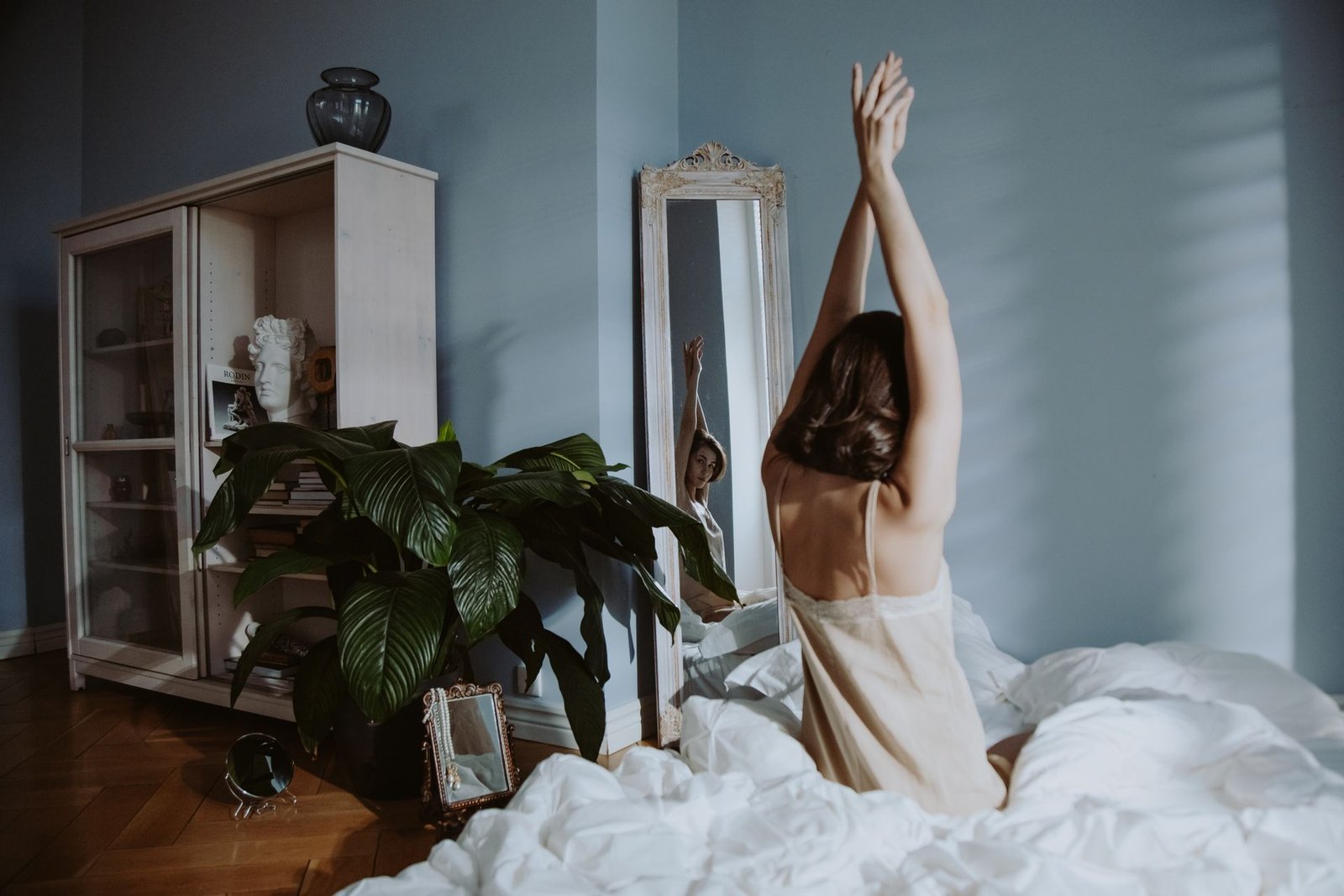 Mulher alongando os braços para cima, sentada na cama, em quarto claro e aconchegante durante a rotina de yoga para o sono