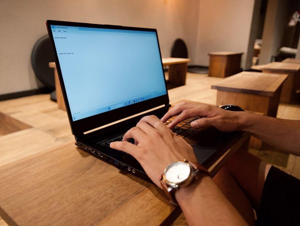 Mãos digitando em notebook sobre mesa de madeira, com relógio de pulso visível, representando o foco profundo em ambiente de trabalho