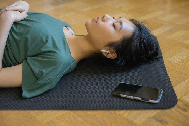 Mulher deitada em tapete de yoga com os olhos fechados, celular ao lado, em pausa de desconexão digital