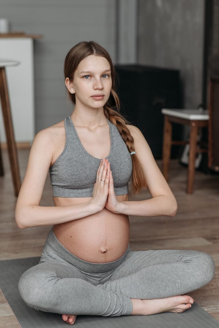 Gestante sentada em pose de meditação praticando pranayama, mãos em Anjali Mudra sobre o ventre